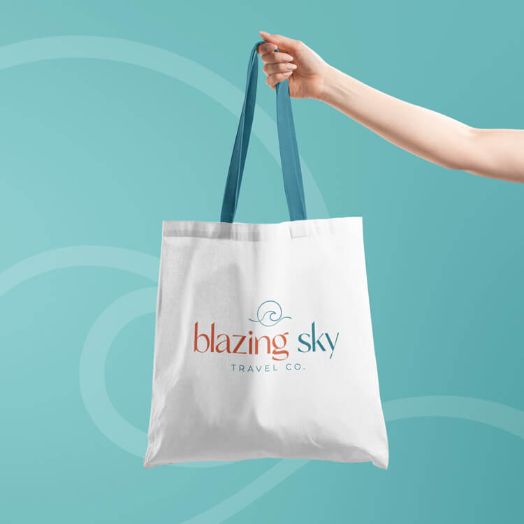 A hand holding a tote bag with the logo on the front on a blue background.