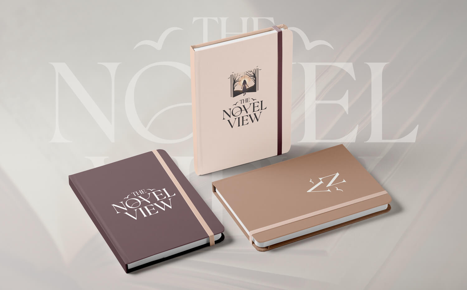 Three hardcover notebooks in beige and brown tones, featuring "The Novel View" logos on their covers, are displayed on a soft, blurred background.