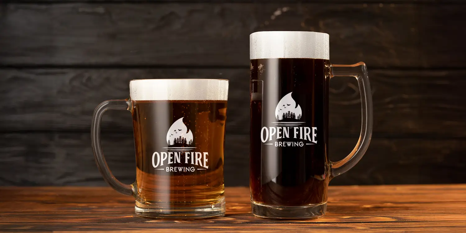 The Open Fire Brewing logo on two different sized beer glass on a wood table.